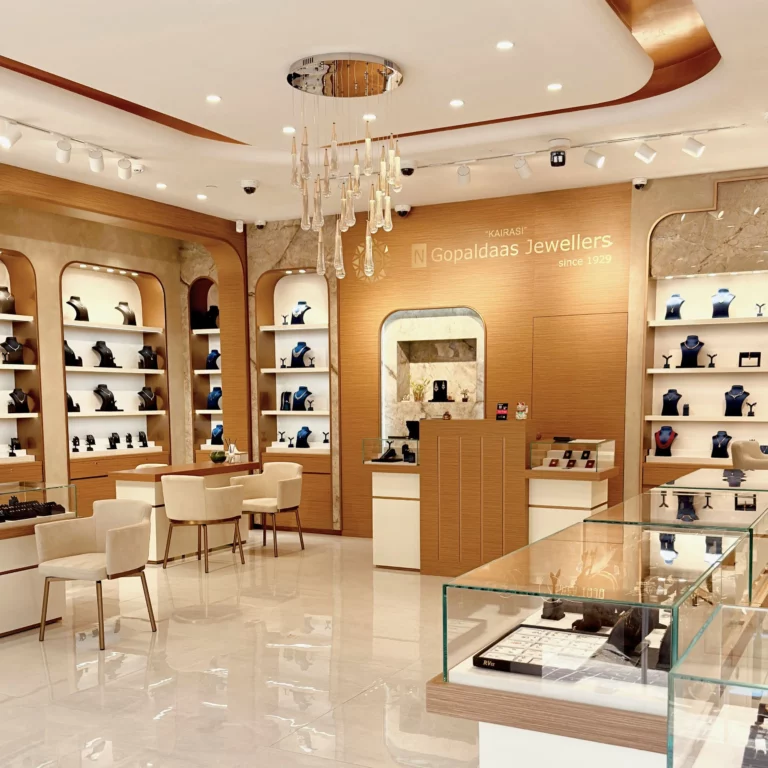 Interior of a jewelry store with glass display cases, necklace busts on shelves, and a cascading chandelier overhead.
