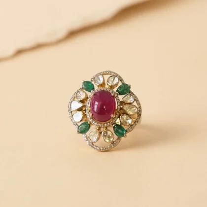 Gold ring with a large pink oval ruby centerpiece, surrounded by diamonds and green emerald-like stones on a circular setting.
